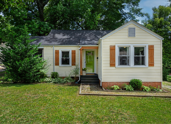 Small cottage-style home in East Greenwich RI with cream siding, wood shutters, and green front door