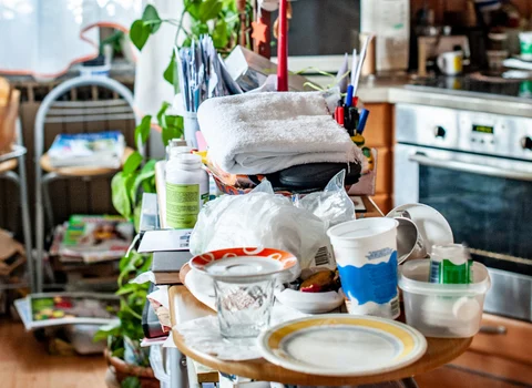 Cluttered kitchen table piled with dishes and household items in a hoarder house in Rhode Island — We Pay More Properties buys hoarder homes as-is