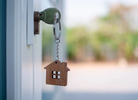 House key with wooden home keychain in door lock — sell your Rhode Island home with an existing mortgage through We Pay More Properties