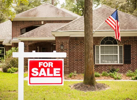 For Sale sign in front of brick home with American flag in Rhode Island — We Pay More Properties helps out-of-state heirs sell inherited houses fast for cash