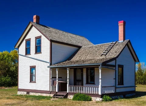 Older white farmhouse with covered porch and two chimneys in Rhode Island — guidance on selling your house before or after divorce from We Pay More Properties