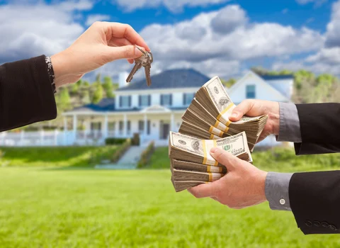 Person handing house keys in exchange for cash in front of a blue colonial home in Rhode Island — iBuyer vs local cash buyer comparison from We Pay More Properties