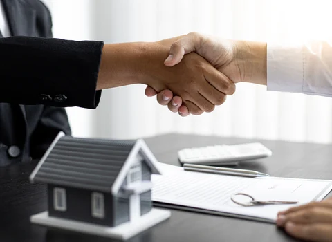 Two people shaking hands over a real estate contract with a house model on the desk in Rhode Island — fair cash offer alternative to We Buy Ugly Houses from We Pay More Properties
