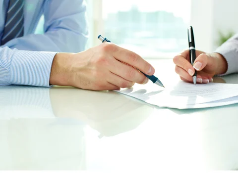 Two people reviewing and signing documents at a desk in Rhode Island — home seller's tax guide covering transfer tax, property taxes, and capital gains from We Pay More Properties