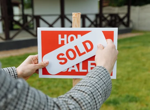 Person placing a sold sign over a home for sale sign in Rhode Island — We Pay More Properties helps families sell a deceased parent's house fast for cash
